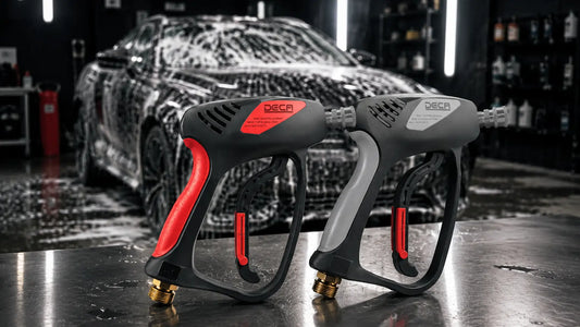 Two DECA high-pressure spray guns—one in classic red and black, the other in industrial gray and black—standing side-by-side in front of a black car covered in thick car wash foam.
